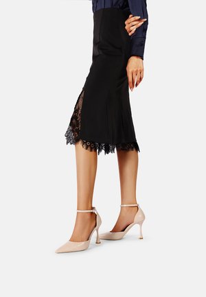 Gonna a matita nera con bordo in pizzo all'orlo, abbinata a décolleté color nudo con cinturino alla caviglia, tacco a spillo sottile e punta affusolata.