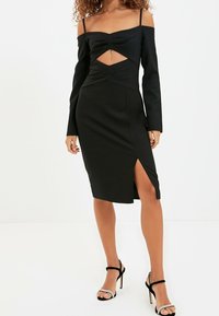 Černé šaty s dlouhými off-shoulder rukávy, nařaseným předním dílem a výřezem. Střední délky s bočním rozparkem, vyrobené z hladkého materiálu.