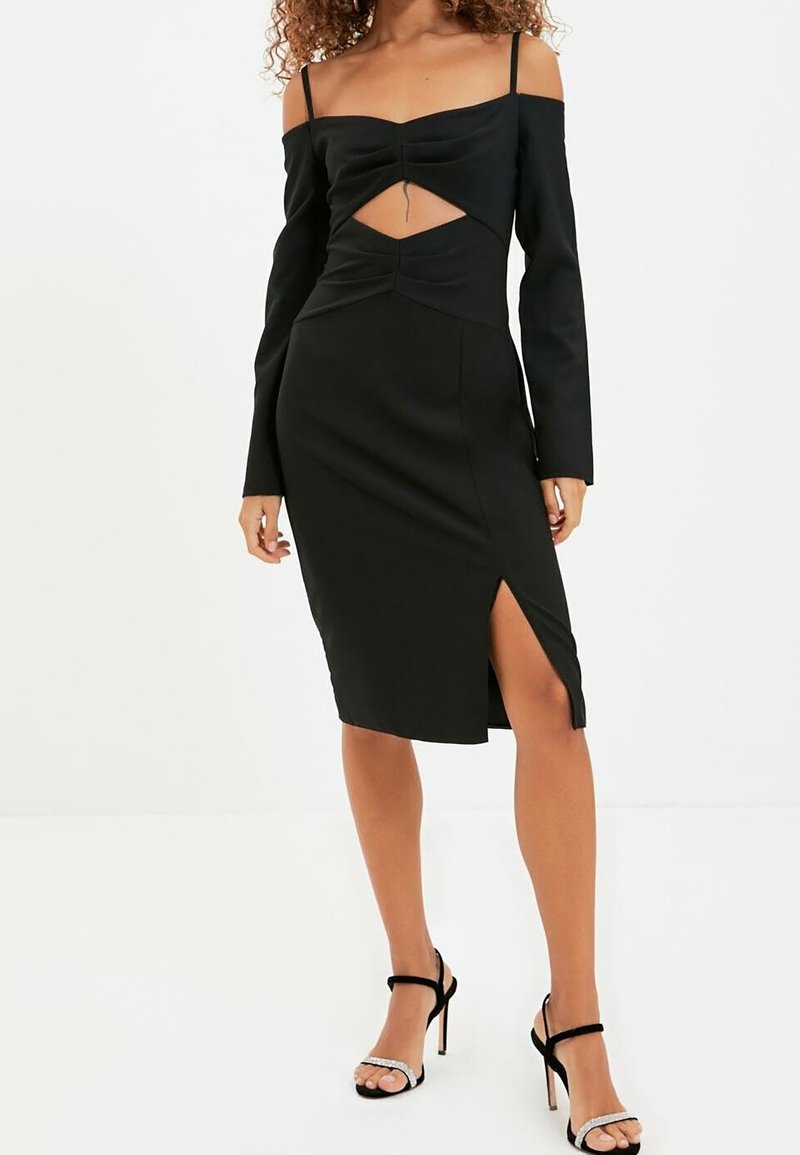 Černé šaty s dlouhými off-shoulder rukávy, nařaseným předním dílem a výřezem. Střední délky s bočním rozparkem, vyrobené z hladkého materiálu.