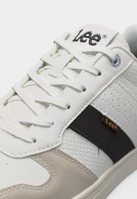 Λευκό αθλητικό παπούτσι με το λογότυπο Lee στη γλώσσα και την πλευρά, με λευκά κορδόνια, δέρμα με τρύπες και μπεζ σουέντ λεπτομέρειες.