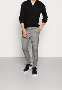 Black ribbed sweater, gray checkered tapered pants, and black sneakers. Sweater features a zip collar; shoes have white soles.