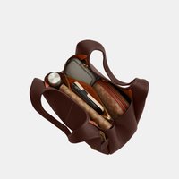Borsa a mano in pelle marrone aperta per mostrare all’interno una bottiglia d’acqua, un portafoglio, un telefono e due pochette con cerniera.