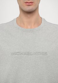 Szürke pamut pulóver kerek nyakkal, kiemelkedő "MICHAEL KORS" logóval a mellkason. Sima textúra.