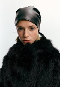 Musta nahkainen huivi, jossa on sileä pinta, päällä musta tekoturkistakki, jossa on pitkät, pehmeät kuidut. Yksinkertainen muotoilu ja tummat sävyt.