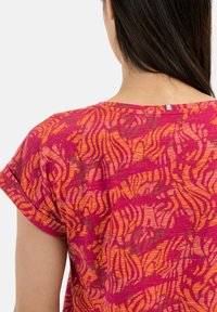 Top de manga corta en un vibrante color rosa con patrones abstractos en naranja y rojo; cuenta con un cuello redondo y un sutil detalle en la parte posterior.