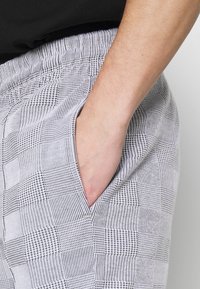 Herren Karo-Shorts mit strukturiertem Muster, ausgestattet mit einem flexiblen Bund und seitlichen Taschen, in Schwarz-weiß.