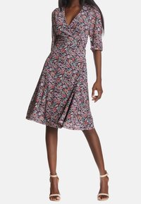 Květinové zavinovací šaty v černé barvě s růžovými a červenými květinami. Krátké rukávy, V-výstřih, délka k kolenům a áčkový silueta s jemným leskem.