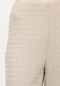 Κοντινή λήψη μπεζ υφασμάτινου παντελονιού με υφή, λεπτό κυματιστό μοτίβο και ελαστική μέση.