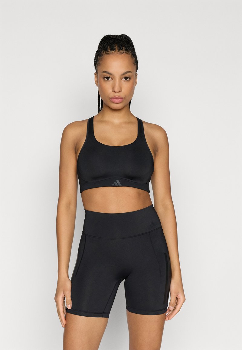 Czarny sportowy biustonosz i szorty z wysokim stanem wykonane z gładkiego, elastycznego materiału. Biustonosz ozdobiony jest detalem z logo, a szorty mają kieszenie.