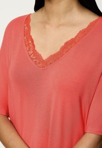 Koralowa bluzka z dekoltem w serek i krótkimi rękawami, z koronkowym wykończeniem wzdłuż dekoltu. Miękka tkanina o gładkiej fakturze i luźnym kroju.