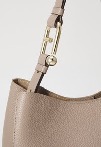 Sac fourre-tout en cuir marron clair avec une finition texturée, doté d'une fermeture métallique dorée et d'un détail de sangle réglable.
