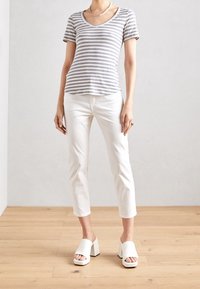 Striped gray and white short-sleeved top with a V-neck, paired with white cropped pants and white block-heeled mules on wooden floor.