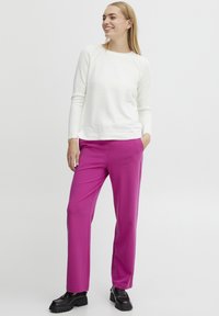 Pull en tricot blanc à manches longues, associé à un pantalon tailleur rose vif et des mocassins noirs épais. Design simple et texture lisse.