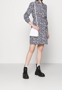 Abito camicia con stampa floreale in blu navy e bianco, dotato di maniche lunghe e una cintura in vita. Abbinato a una borsa bianca piccola e stivaletti neri chunky alla caviglia.