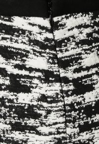 Gebreide jurk in zwart en wit met een textuur, abstract patroon. Heeft een zwart bovenstuk en een zichtbare ritsdetail aan de achterkant.