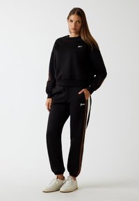 Zwart sweatshirt en broekset, voorzien van een ronde hals, elastische manchetten en zijstrepen in bruin, stijlvol gecombineerd met witte sneakers.