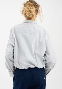 Camisa de botones a rayas en azul claro y blanco, con collar y un corte relajado. Combinada con pantalones azul marino, que presentan una textura suave.