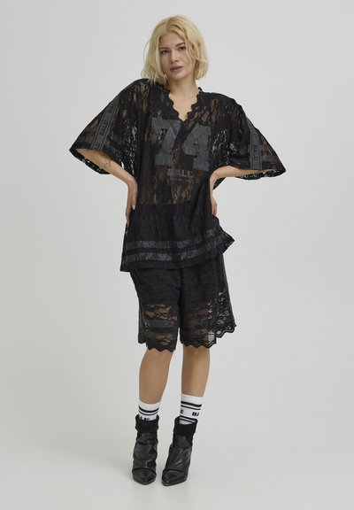 Haut oversize en dentelle noire avec le graphisme "74", assorti à un short assorti. Caractéristiques : texture transparente, bords festonnés et chaussettes sportives.