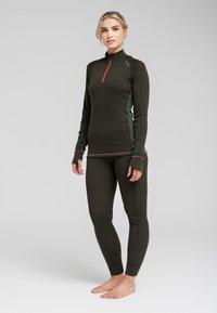 Mørkegrøn langærmet termotrøje med halvlynlås og kontrasterende rød lynlås; parret med matchende tætsiddende termoleggings. Glat tekstur, atletisk design.