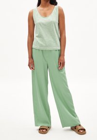 Débardeur à rayures vertes associé à un pantalon ample vert uni et des sandales plates marron, offrant une coupe décontractée et un tissu doux.