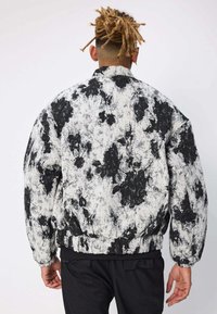 Veste bomber à motifs floraux en noir et blanc, avec une coupe décontractée, des poignets et un ourlet côtelés, fabriquée à partir d'un tissu doux et texturé.