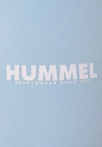 Lichtblauwe sportkledingstof met "HUMMEL" in vette witte letters, met daaronder "SPORTSWEAR SINCE 1923" gedrukt in een kleiner lettertype.