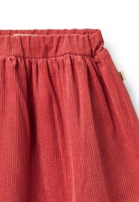 Rød corduroy nederdel med en samlet elastisk talje, der har en vertikal ribbet tekstur og et subtilt mærke på sidesømmen.