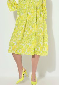 Jasnożółta sukienka w kwiatowy wzór, z rękawami do połowy łokcia, plisowanym krojem, zestawiona z pasującymi żółtymi szpilkami.
