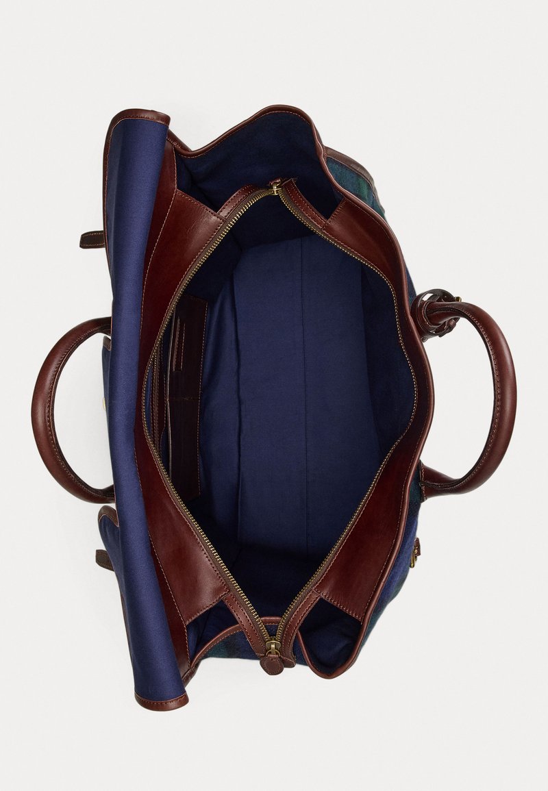 Brown leather tote bag with navy fabric interior, a zip closure, and dual handles, showcasing a spacious, unlined compartment.
