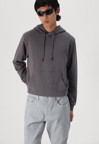 Grå bomullshoodie med frontlomme, hette med snøre og ribbestrikkede mansjetter, paired med lysegrå denimbukser.