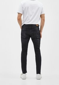 Jeans ajustados negros con una textura suave, con un parche de cuero en la cintura trasera y en los bolsillos traseros, combinados con una camiseta blanca.