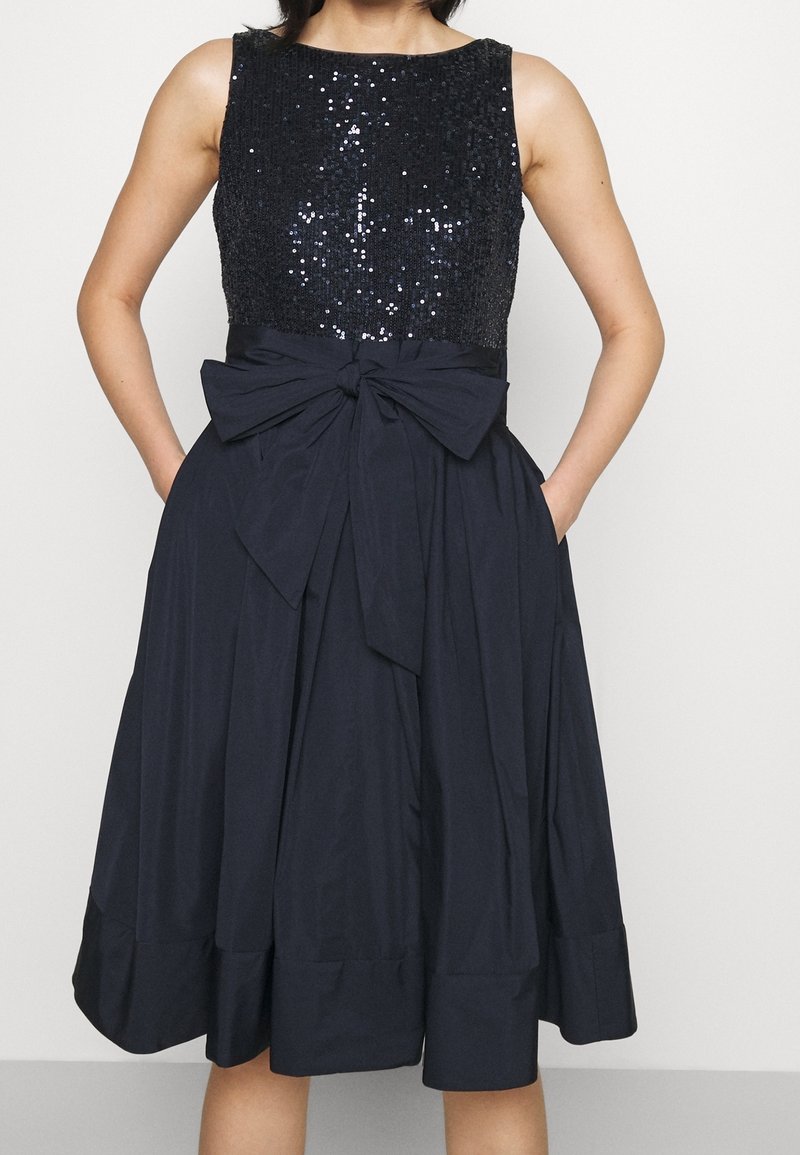 Svart bodice med paljetter, ärmlös design, inringar midja med en stor rosett och en flödande marinblå kjol med sidofickor.