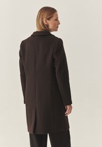 Bruine wollen jas met een getailleerde pasvorm, notch-kraag en een enkele rugventilatie. De gladde textuur en het middellange ontwerp bieden warme bescherming.