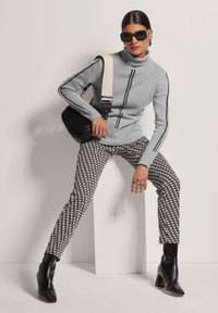 Grau gestrickter Rollkragenspullover mit schwarzen Streifen, texturiertem Design; gemusterte schwarz-weiße Hose; schwarze Stiefeletten; Umhängetasche mit Träger.