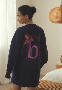 Navy oversized sweatshirt dress with a large pink letter "b" and floral design on the back. Soft fabric, long sleeves, casual silhouette.