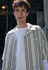 Chemise à manches courtes rayée en vert pâle, gris et blanc. Comprend un devant boutonné, une poche poitrine et un tissu en coton doux.