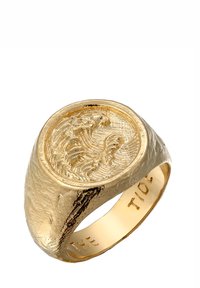 Arany színű pecsétgyűrű textúrált, organikus dizájnnal. Az ékszer tetején egy kiemelkedő hullám mintázat található, az belsejében pedig a "THE TIDE" felirat.