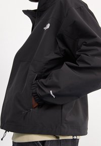 Chaqueta cortavientos negra con puños elásticos, bolsillos laterales y logo en el pecho y la manga. Tejido liso, corte holgado, dobladillo ajustable.