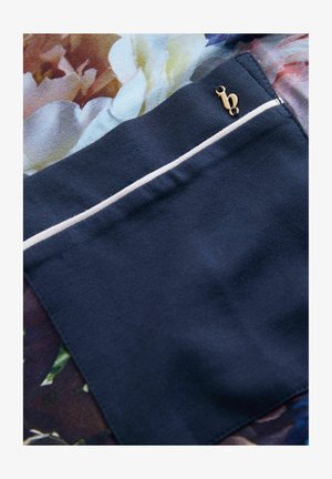 Námořnická látka s květinovým vzorem, obsahující malou kapsu s bílým lemováním a zlatým akcentem. Hladká textura po celé ploše.