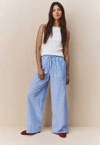 Lahka bela top iz rebraste tkanine, združena s širokimi modrimi hlačami v karo vzorcu, z vrvico v pasu in teksturirano tkanino.