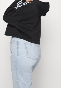 Felpa nera corta con strisce orizzontali bianche sulle maniche, abbinata a jeans in denim azzurro chiaro a vita alta con tasche posteriori.