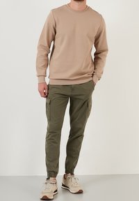 Felpa beige con girocollo, abbinata a pantaloni cargo conici verde oliva. Tessuto leggermente strutturato, con polsini elastici e tasche laterali.