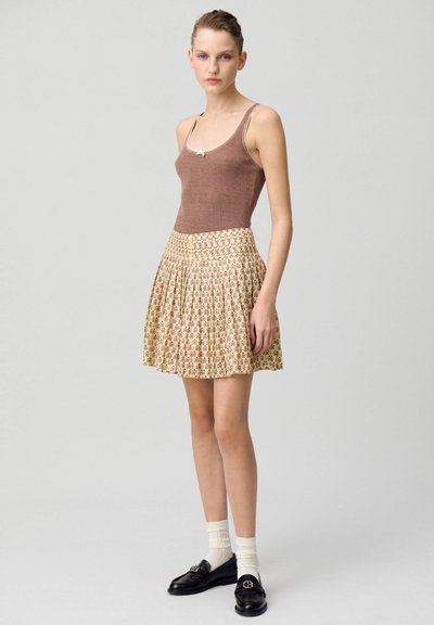Top de tirantes marrón a rayas combinado con una falda plisada floral en crema. Mocasines negros con detalles en dorado y calcetines blancos completan el atuendo.