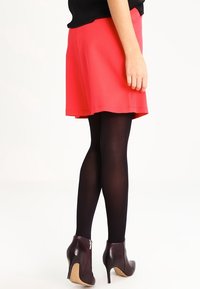 Red A-line skirt paired with black tights and burgundy high-heeled ankle boots, featuring a smooth texture and a simplistic design.