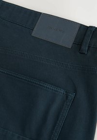 Pantalone tamnoplave boje izrađene od izdržljive tkanine, sa kožnom oznakom na kojoj piše "DENIM SUPPLY", i stražnjim džepom s diskretnim šavovima.