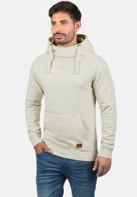 Light beige hoodie made of soft fabric, featuring a large hood, kangaroo pocket, and a small leather label on the front.