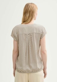 Blouse beige à manches courtes avec un dos plissé, des motifs verticaux noirs et un col arrondi. Tissu doux et léger avec une coupe décontractée.