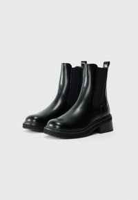 Botas negras de cuero hasta el tobillo con paneles elásticos en los laterales, punta redonda y un tacón ancho. Textura suave con lengüetas en la parte posterior para facilitar su uso.