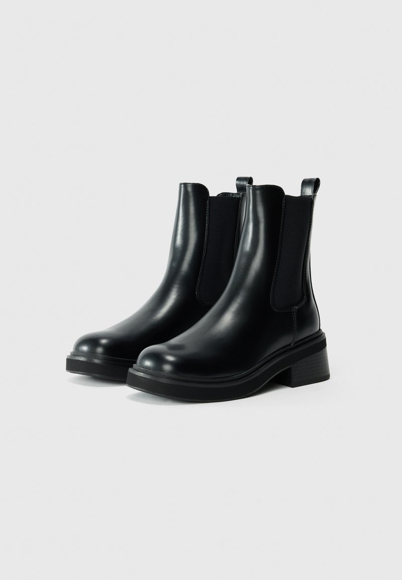 Bottines en cuir noir avec panneaux élastiques sur les côtés, bout rond et talon épais. Texture lisse avec des tirants à l'arrière pour un enfilage facile.