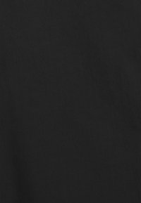 Mies, joka käyttää mustaa v-kaula-aukkoinen lyhythihainen t-paita ja seisoo valkoista taustaa vasten.